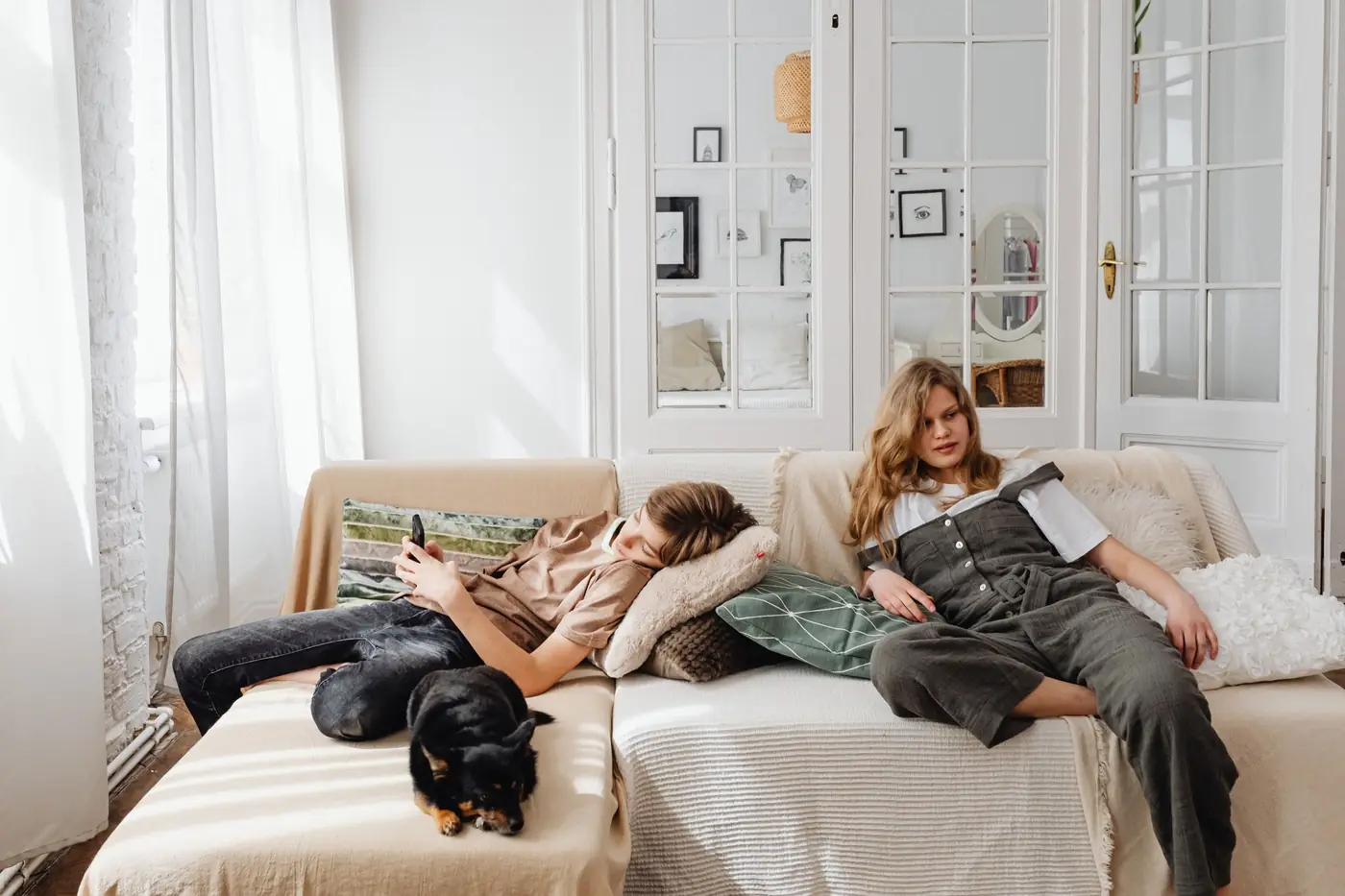 Two teenagers relaxing on a sofa at home with a dog