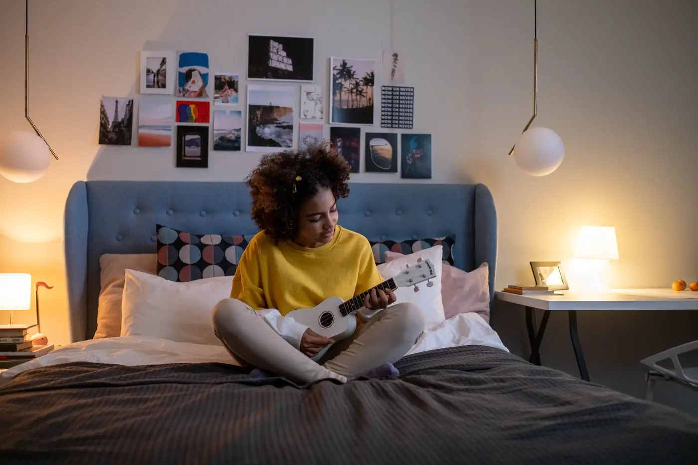 A teenage girl playing the ukulele on her bed in her own room